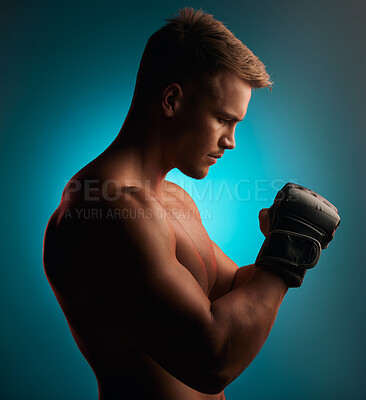 Buy stock photo Shot of a handsome young boxer standing alone and posing against a blue background in the studio