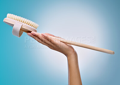 Buy stock photo Cropped shot of an unrecognisable woman holding a body brush against a blue background in the studio