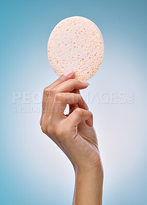 Buy stock photo Cropped shot of an unrecognisable woman holding an exfoliating facial sponge against a blue background in the studio
