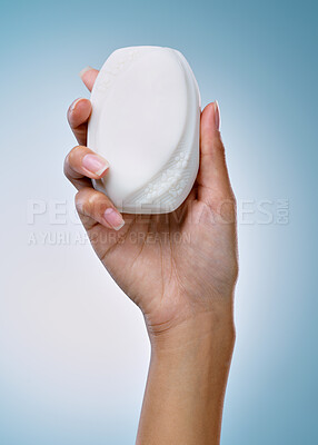 Buy stock photo Cropped shot of an unrecognisable woman holding a bar of soap against a blue background in the studio