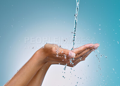 Buy stock photo Cropped shot of an unrecognisable woman cupping her hands to catch water against a blue background in the studio