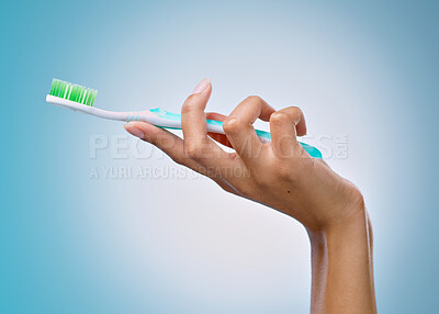 Buy stock photo Cropped shot of an unrecognisable woman holding a toothbrush against a blue background in the studio
