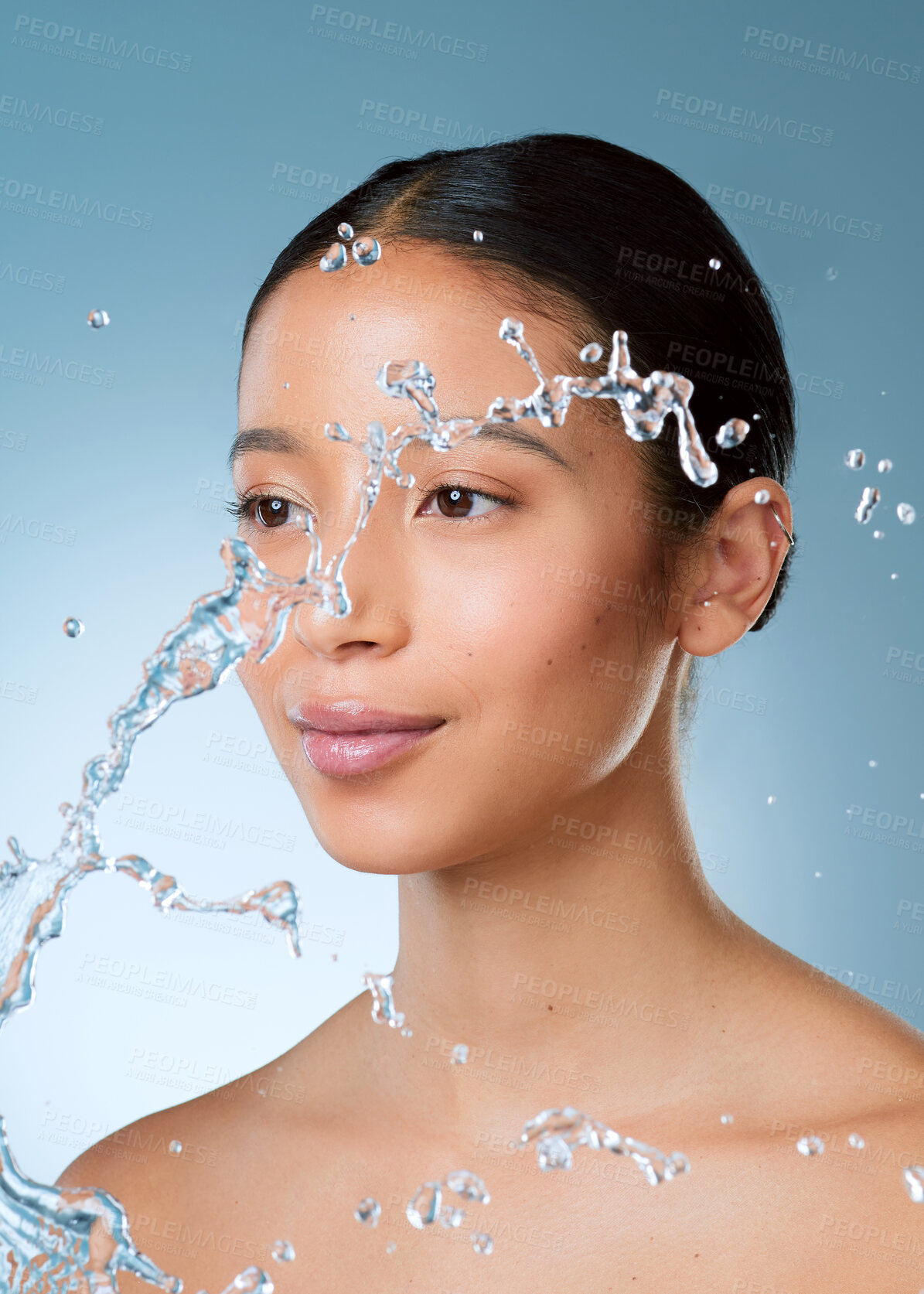 Buy stock photo Shot of an attractive young woman posing against a blue background in the studio while being splashed with water