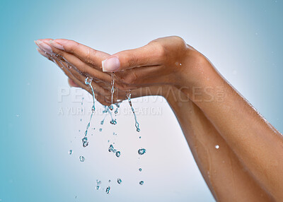Buy stock photo Cropped shot of an unrecognisable woman cupping her hands to catch water against a blue background in the studio