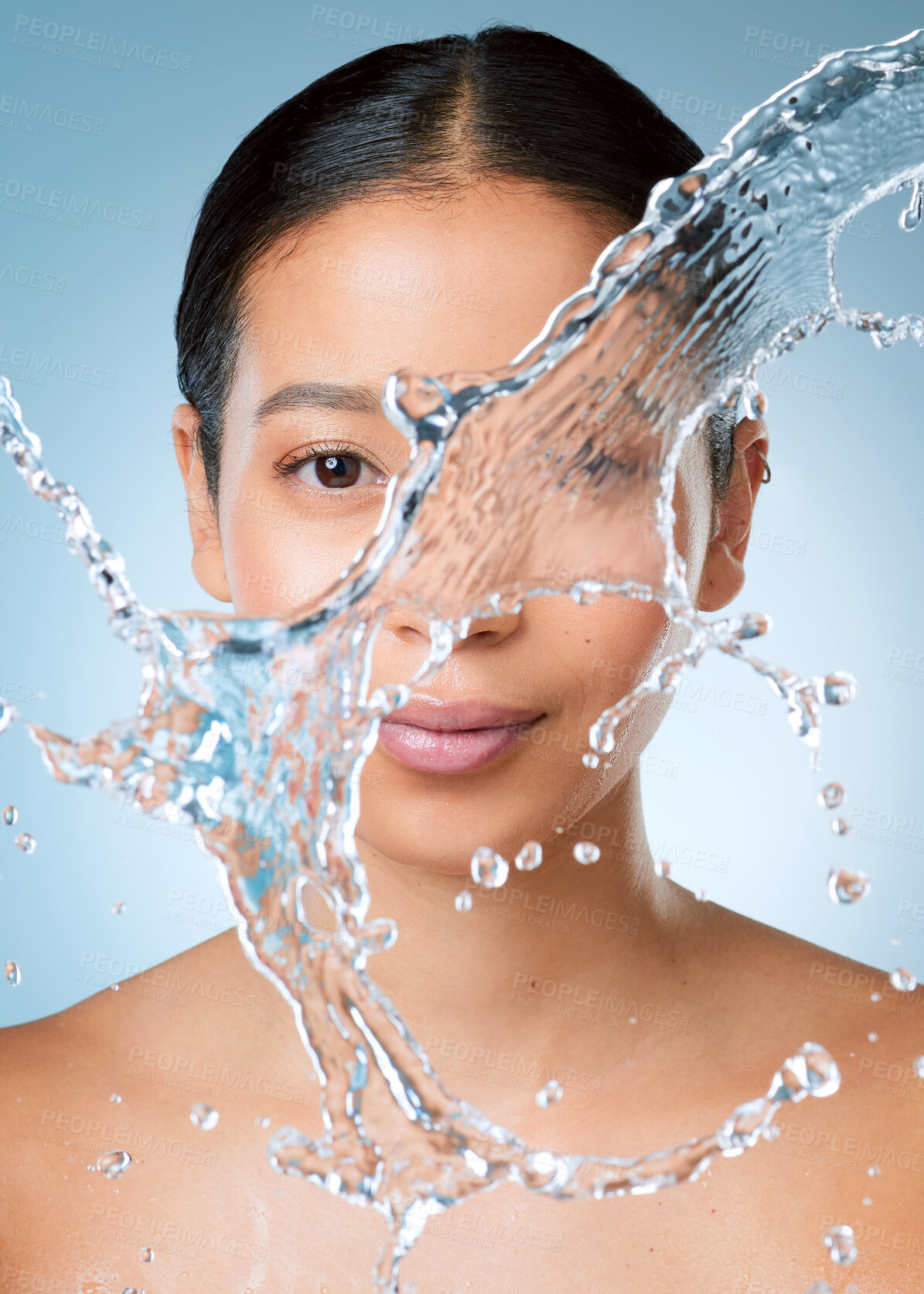 Buy stock photo Shot of an attractive young woman posing against a blue background in the studio while being splashed with water