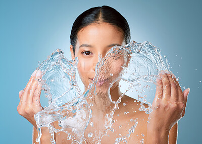 Buy stock photo Shot of an attractive young woman posing against a blue background in the studio and splashing her face with water