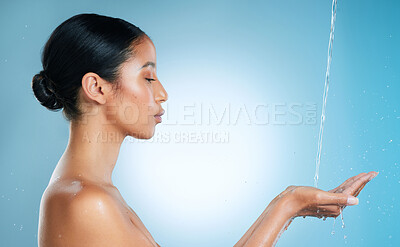 Buy stock photo Shot of an attractive young woman cupping her hands to catch water against a blue background in the studio