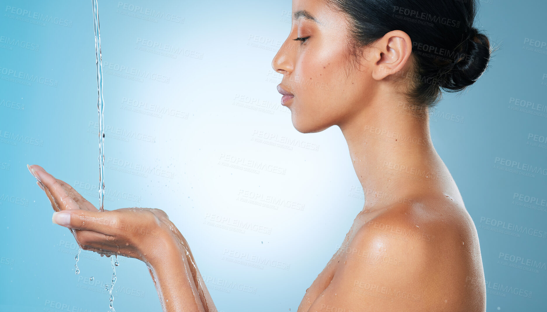 Buy stock photo Cropped shot of an attractive young woman cupping her hands to catch water against a blue background in the studio