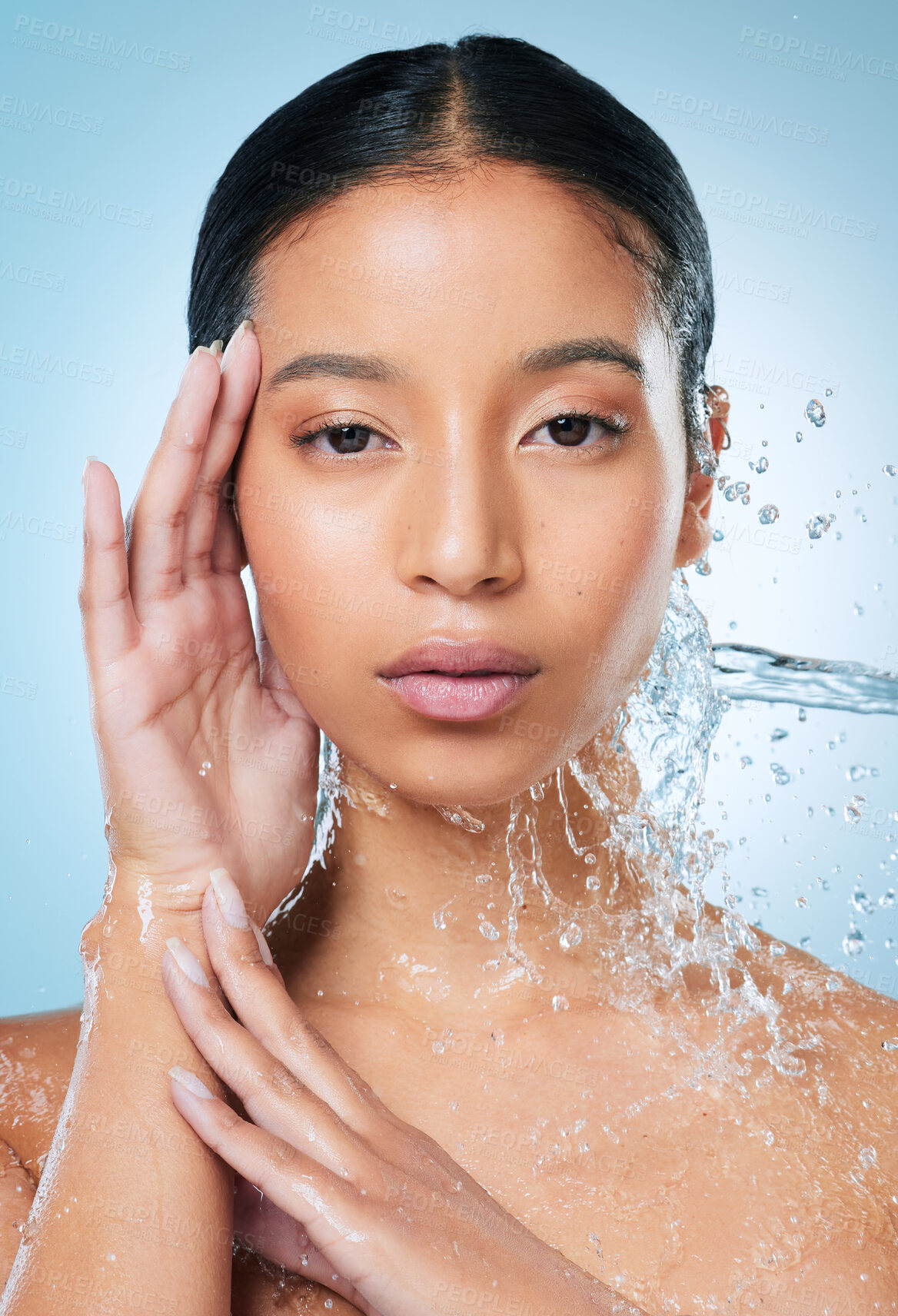 Buy stock photo Shot of an attractive young woman posing against a blue background in the studio while being splashed with water