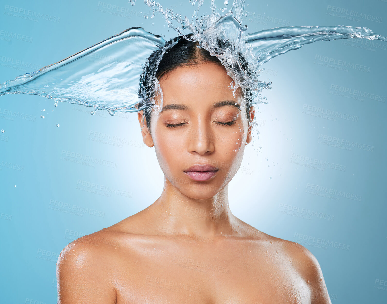 Buy stock photo Shot of an attractive young woman posing against a blue background in the studio while being splashed with water