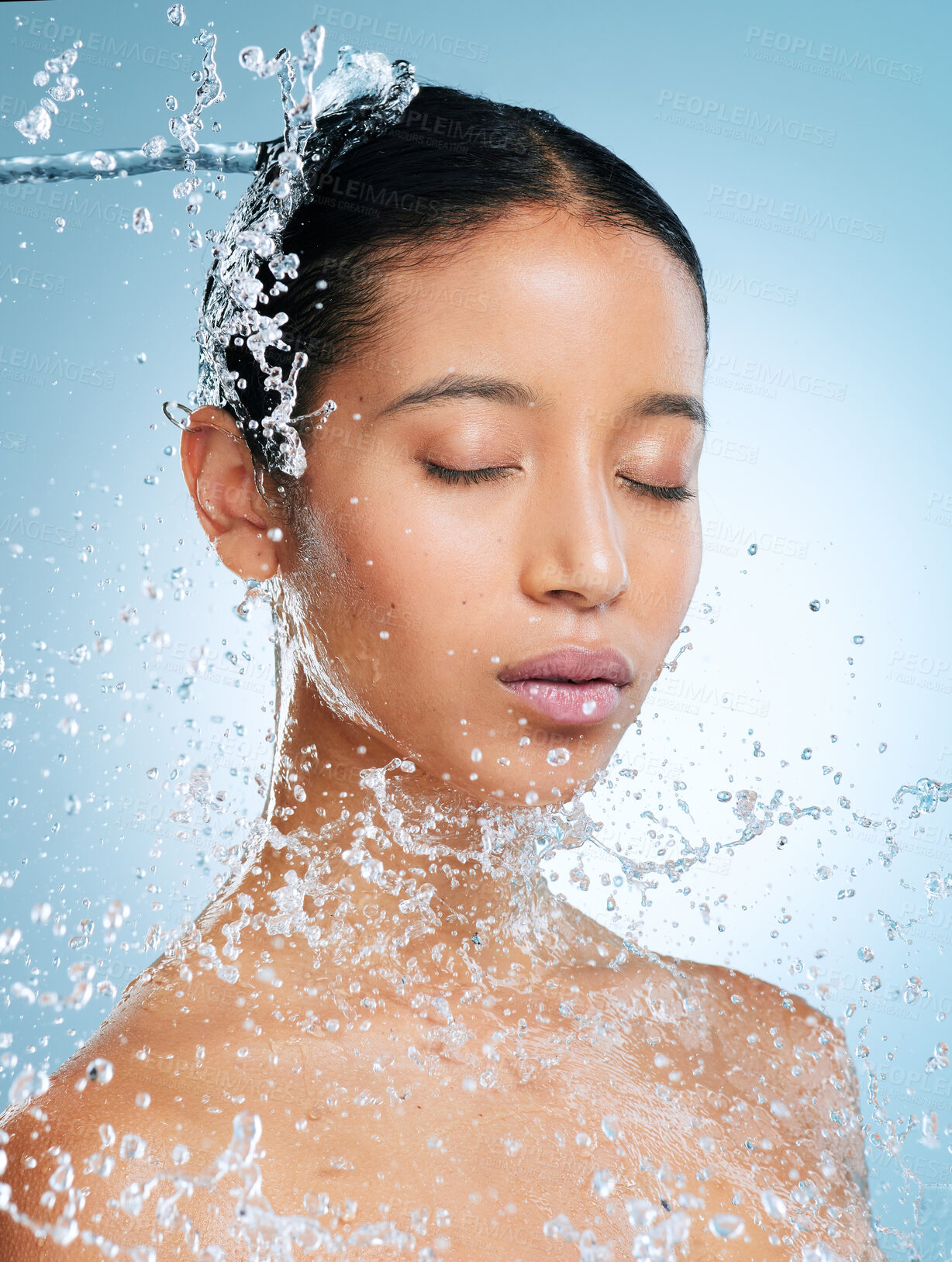 Buy stock photo Shot of an attractive young woman posing against a blue background in the studio while being splashed with water