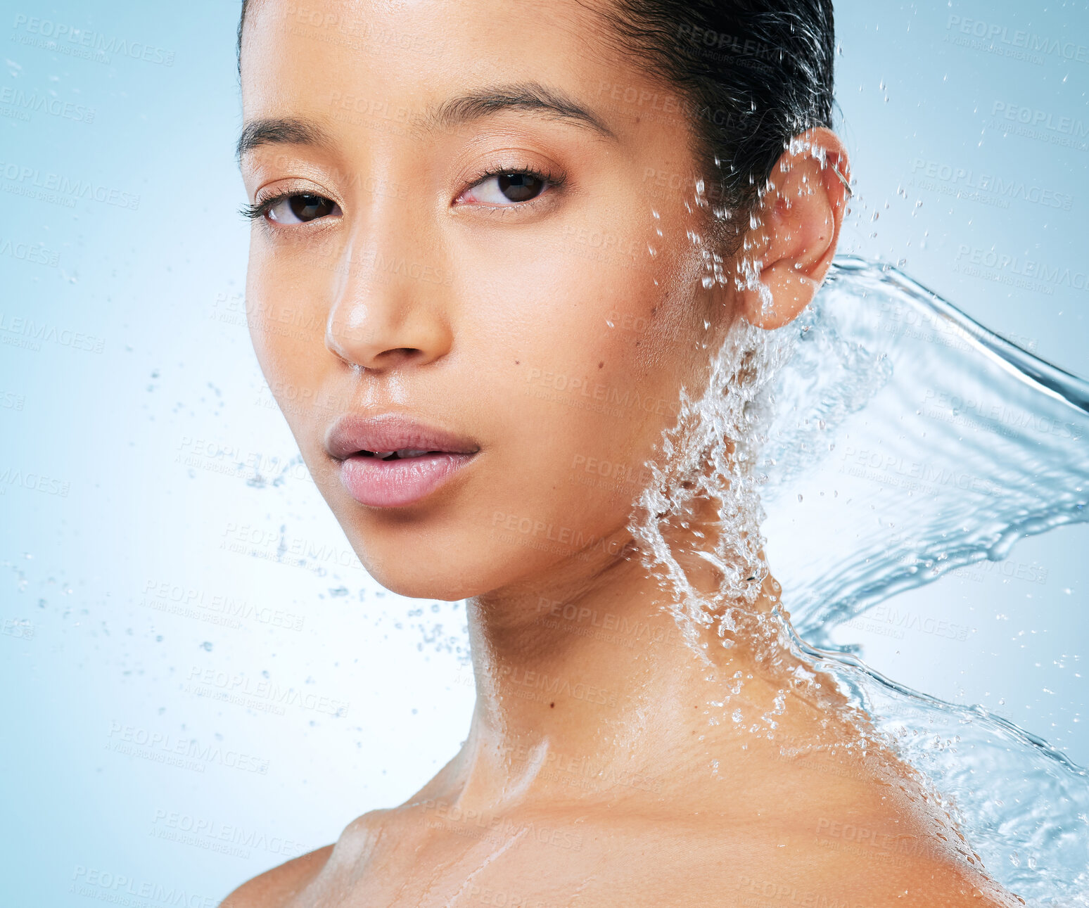 Buy stock photo Shot of an attractive young woman posing against a blue background in the studio while being splashed with water