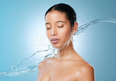 Buy stock photo Shot of an attractive young woman posing against a blue background in the studio while being splashed with water