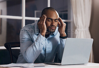 Buy stock photo Shot of a young businessman experiencing a headache while working from home on his laptop at night