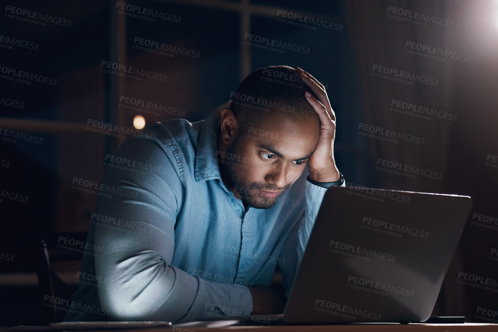 Buy stock photo Shot of a young businessman looking stressed while working on his laptop late at night