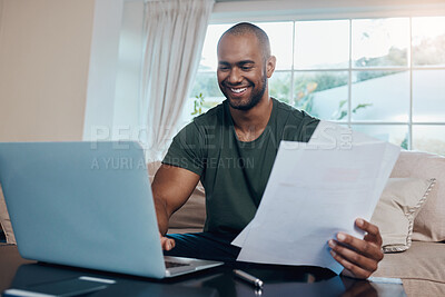 Buy stock photo Shot of a young businessman reading paperwork while working on his laptop