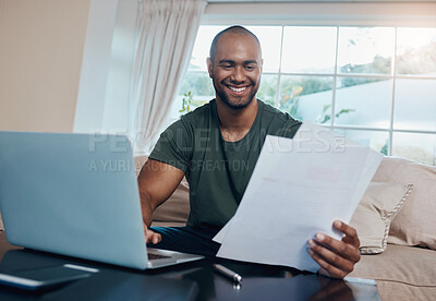 Buy stock photo Shot of a young businessman reading paperwork while working on his laptop