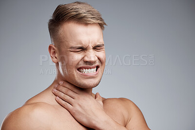 Buy stock photo Studio shot of a muscular young man experiencing neck pain against a grey background