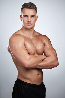 Buy stock photo Studio portrait of a muscular young man posing with his arms crossed against a grey background