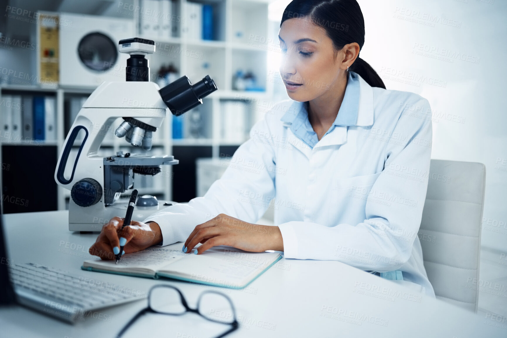 Buy stock photo Shot of a young scientist writing notes while conducting medical research in a laboratory