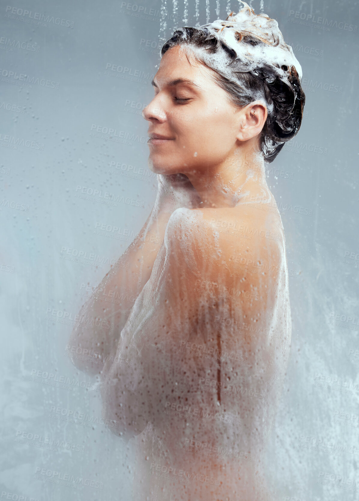 Buy stock photo Shot of a young woman washing her hair in the shower against a grey background