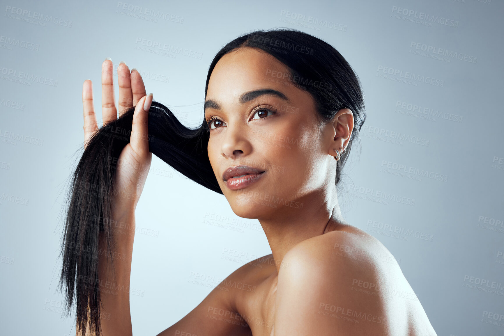 Buy stock photo Studio shot of an attractive young woman holding her hair against a grey background