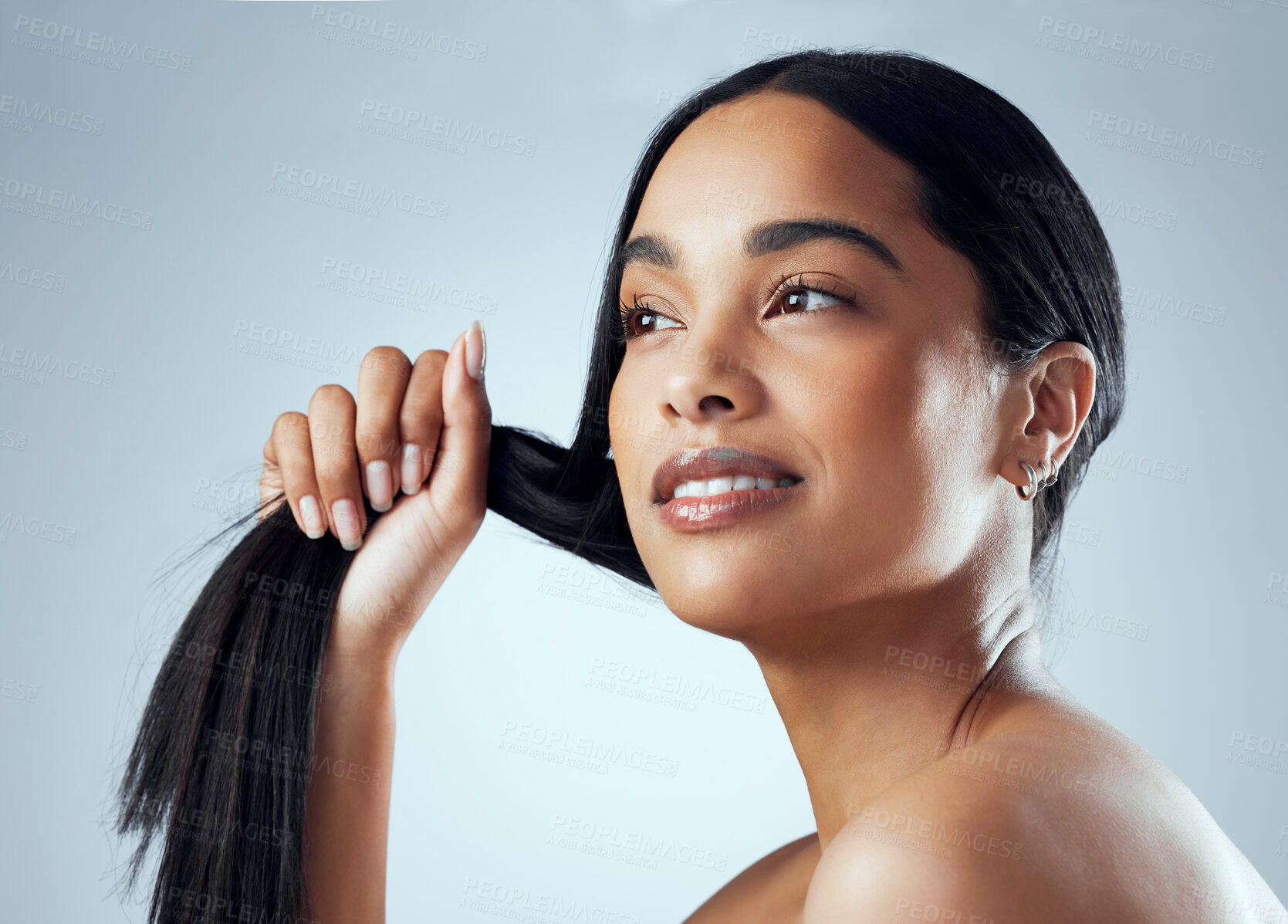 Buy stock photo Studio shot of an attractive young woman holding her hair against a grey background