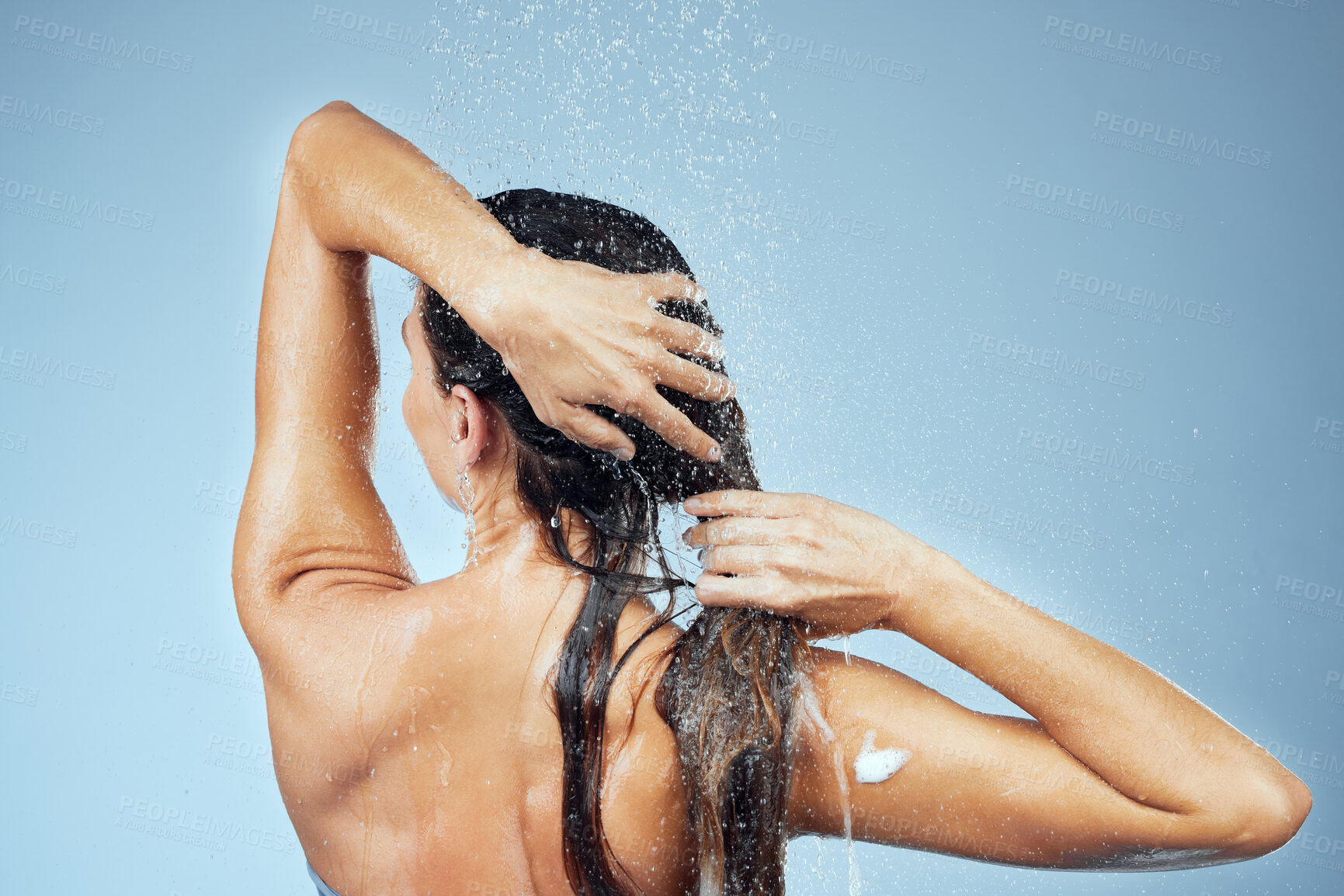 Buy stock photo Studio shot of an attractive young woman washing her hair while taking a shower against a blue background