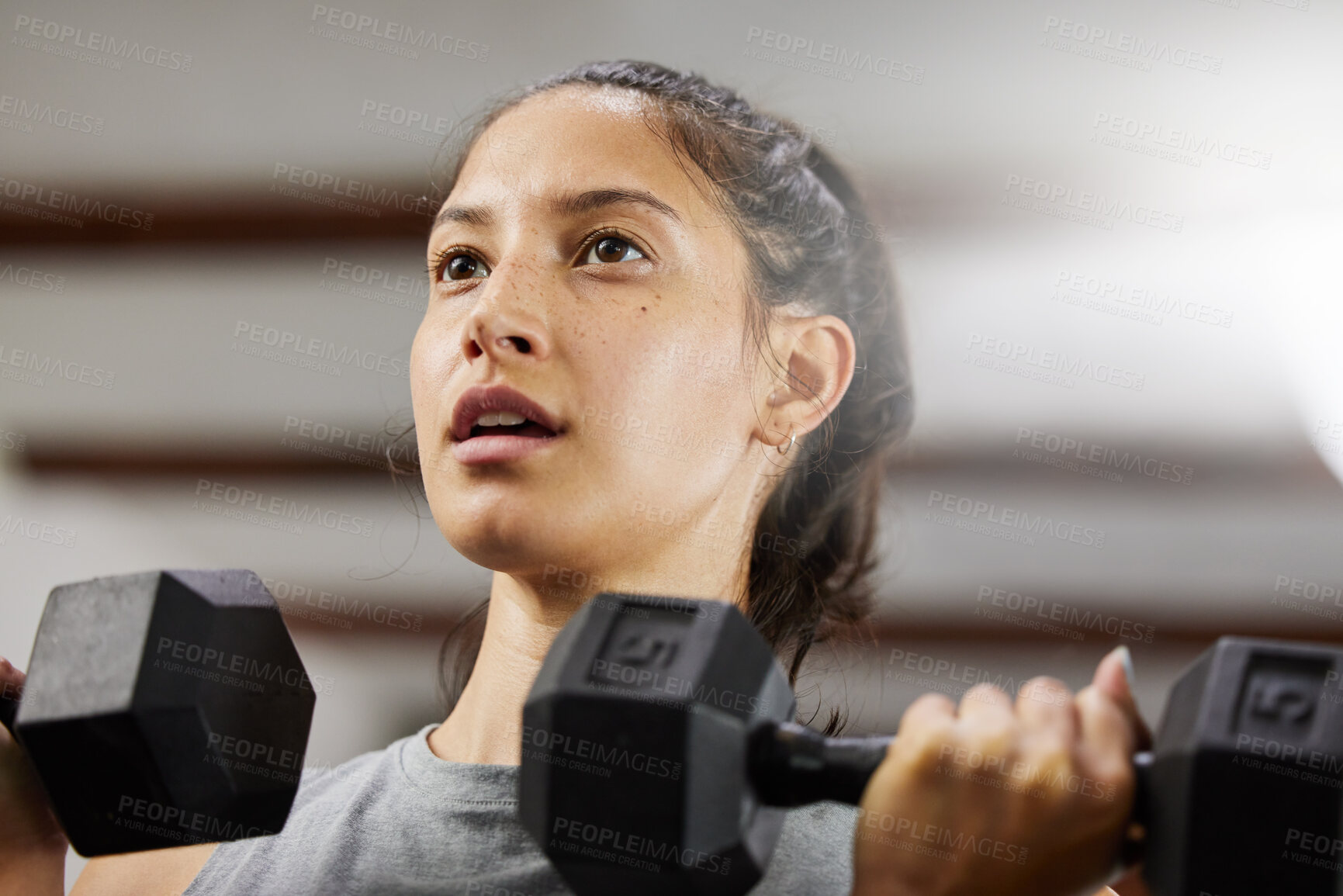 Buy stock photo Low angle shot of a sporty young woman exercising with dumbbells in a gym