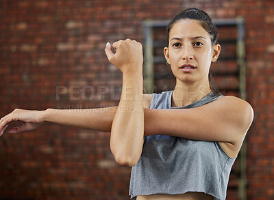 Buy stock photo Shot of a sporty young woman stretching her arms while exercising in a gym