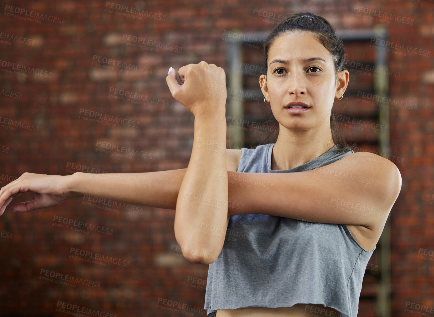 Buy stock photo Shot of a sporty young woman stretching her arms while exercising in a gym