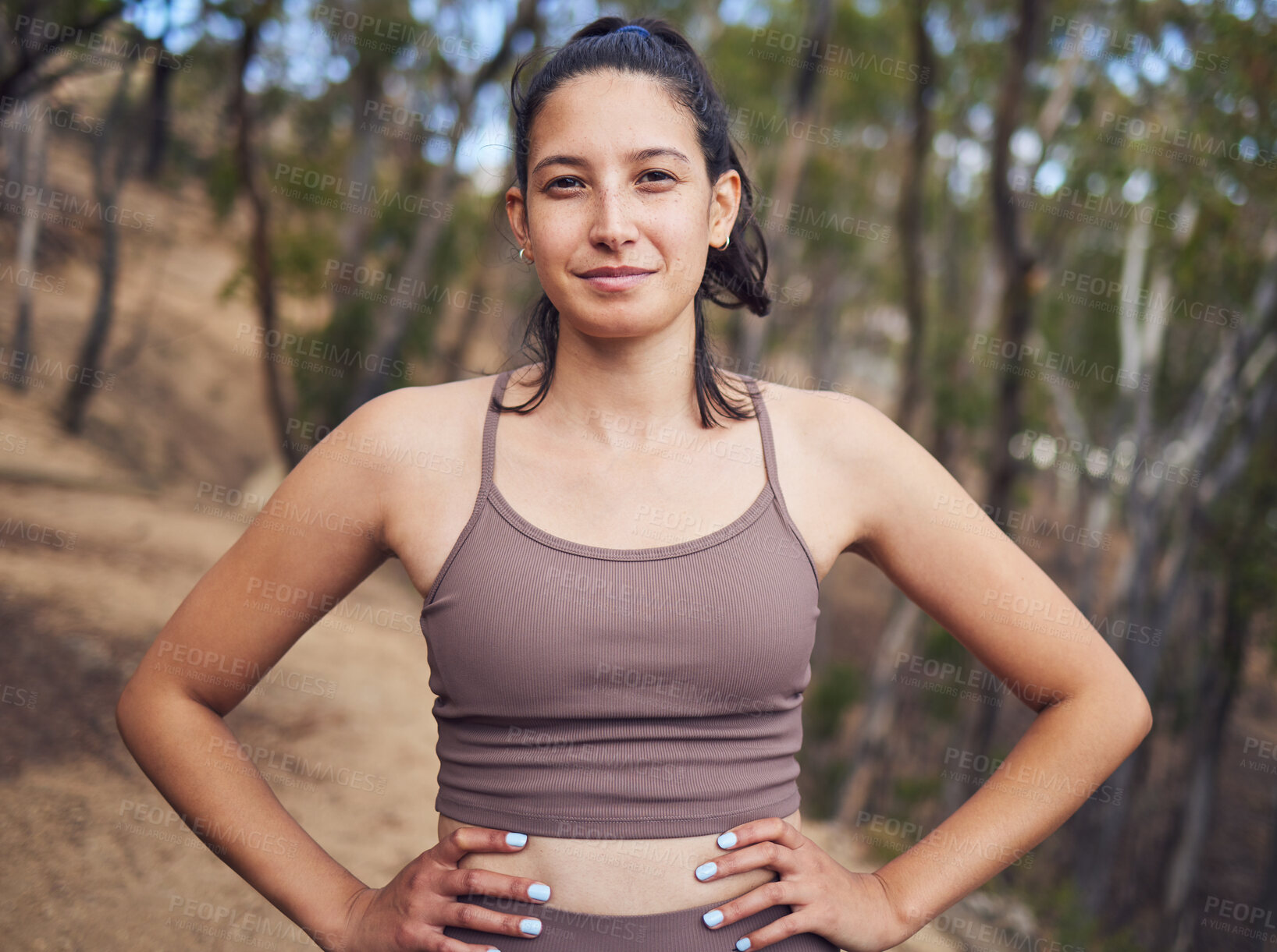 Buy stock photo Portrait of a sporty young woman standing with her hands on her hips while exercising outdoors