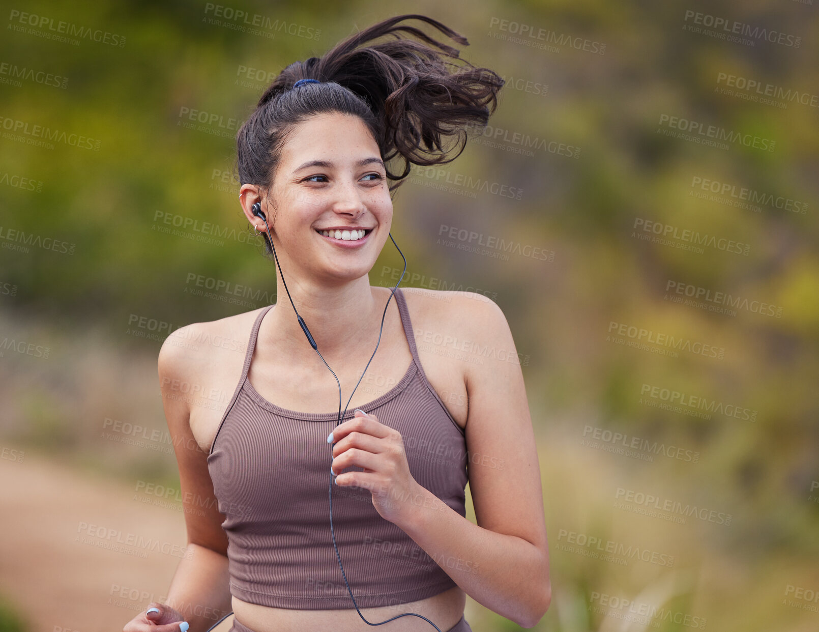 Buy stock photo Shot of a sporty young woman wearing earphones while running outdoors