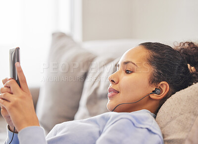 Buy stock photo Cropped shot of an attractive young woman listening to music and texting while relaxing at home