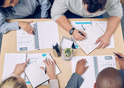 Buy stock photo High angle shot of a group of unrecognizable businesspeople looking over paperwork while sitting around a table in the boardroom