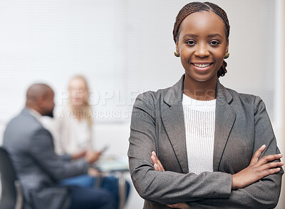 Buy stock photo Portrait of a confident young businesswoman standing with her arms crossed in an office with her colleagues in the background