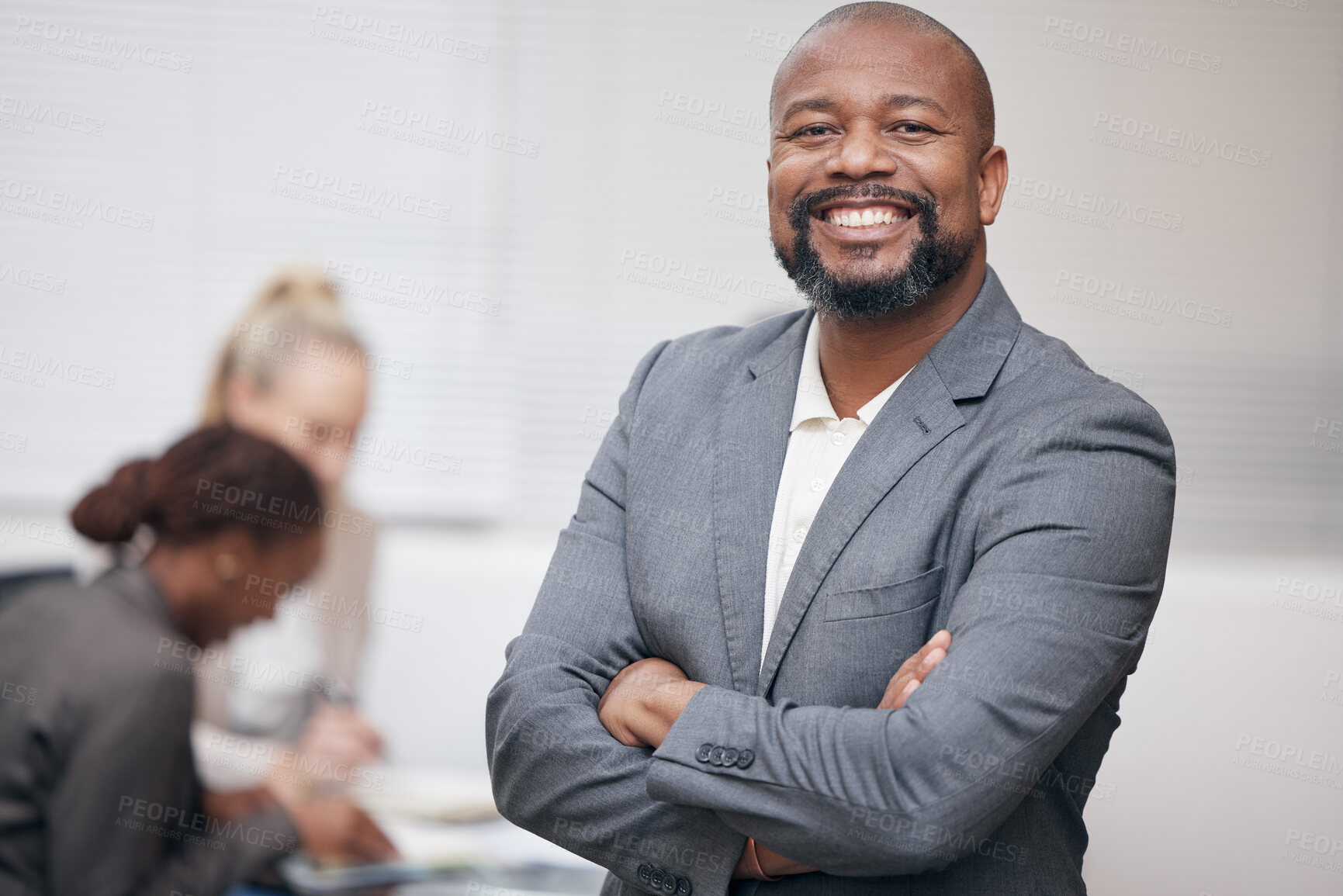 Buy stock photo Portrait of a confident mature businessman standing with his arms crossed in an office with his colleagues in the background