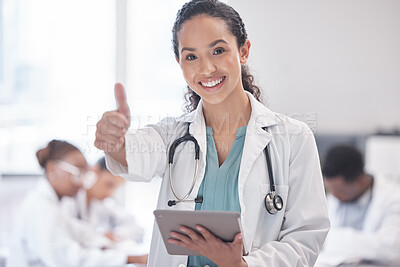Buy stock photo Cropped portrait of an attractive young female doctor giving thumbs up and using a tablet while standing in the boardroom with her colleagues in the background