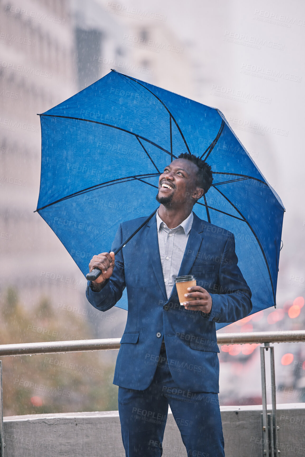 Buy stock photo Shot of a young businessman holding an umbrella in the rain against a city background