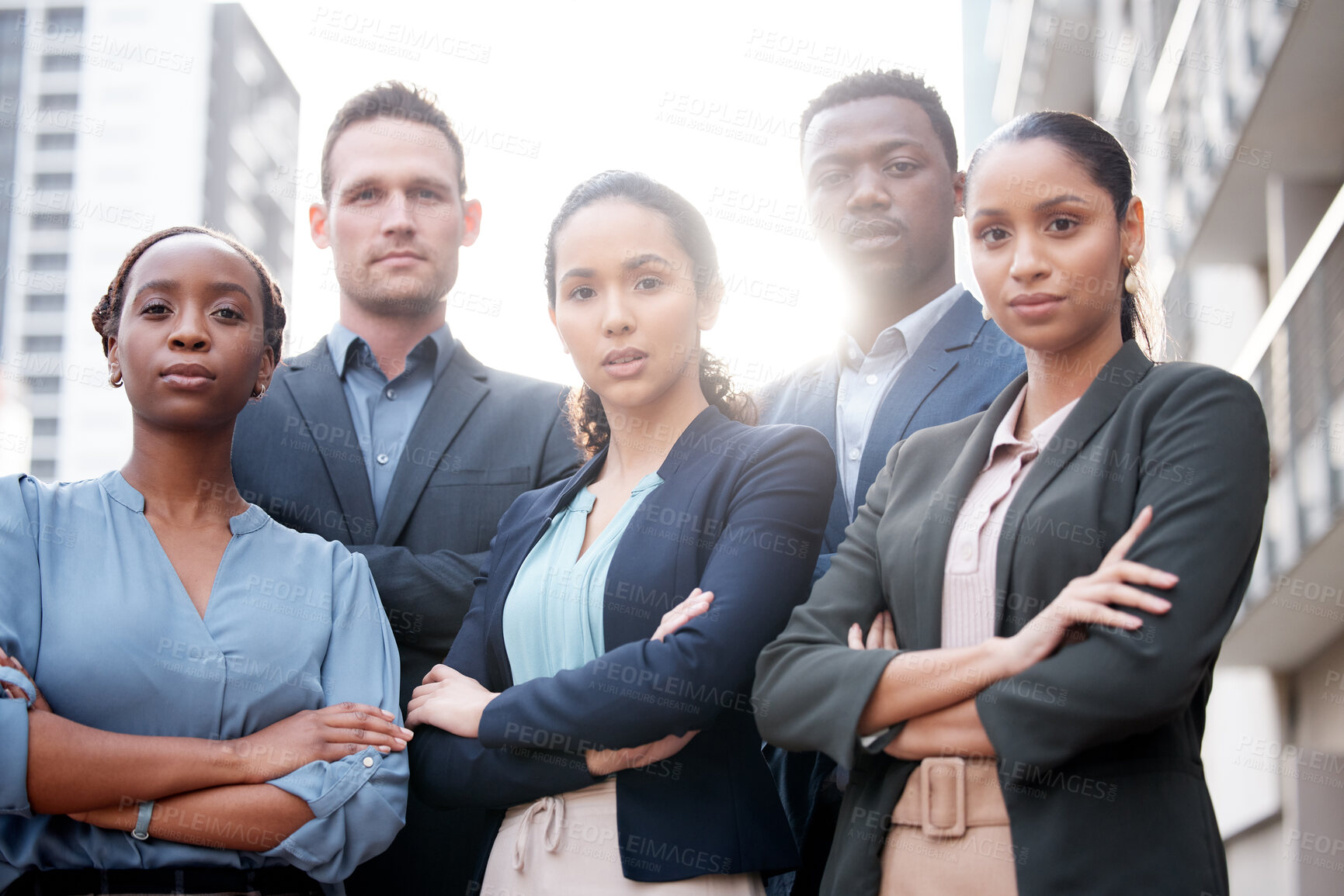 Buy stock photo Shot of a group of young businesspeople standing with their arms crossed against a city background