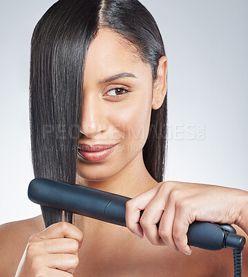Buy stock photo Shot of an attractive young woman using a hair straightener to straighten her hair in the studio