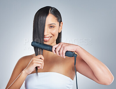 Buy stock photo Shot of an attractive young woman standing alone and using a hair straightener to straighten her hair in the studio