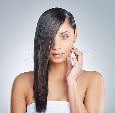 Buy stock photo Shot of a young woman standing alone and posing with her hair covering half of her face in the studio