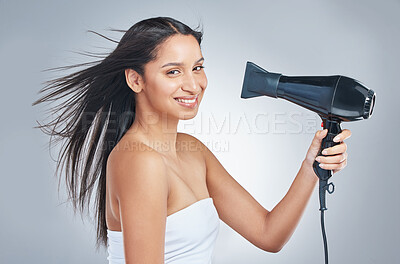 Buy stock photo Shot of an attractive young woman standing alone and using a hairdryer in the studio