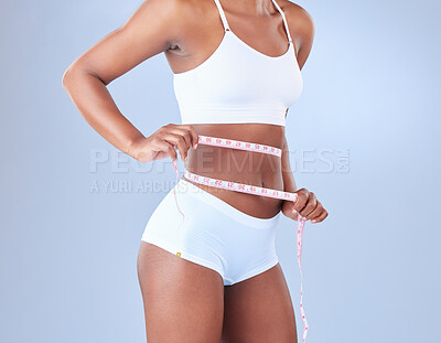 Buy stock photo Woman, waist and weight loss with tape measure in underwear on a blue studio background. African, female person or young model checking stomach size in diet, fitness or slim body from nutrition