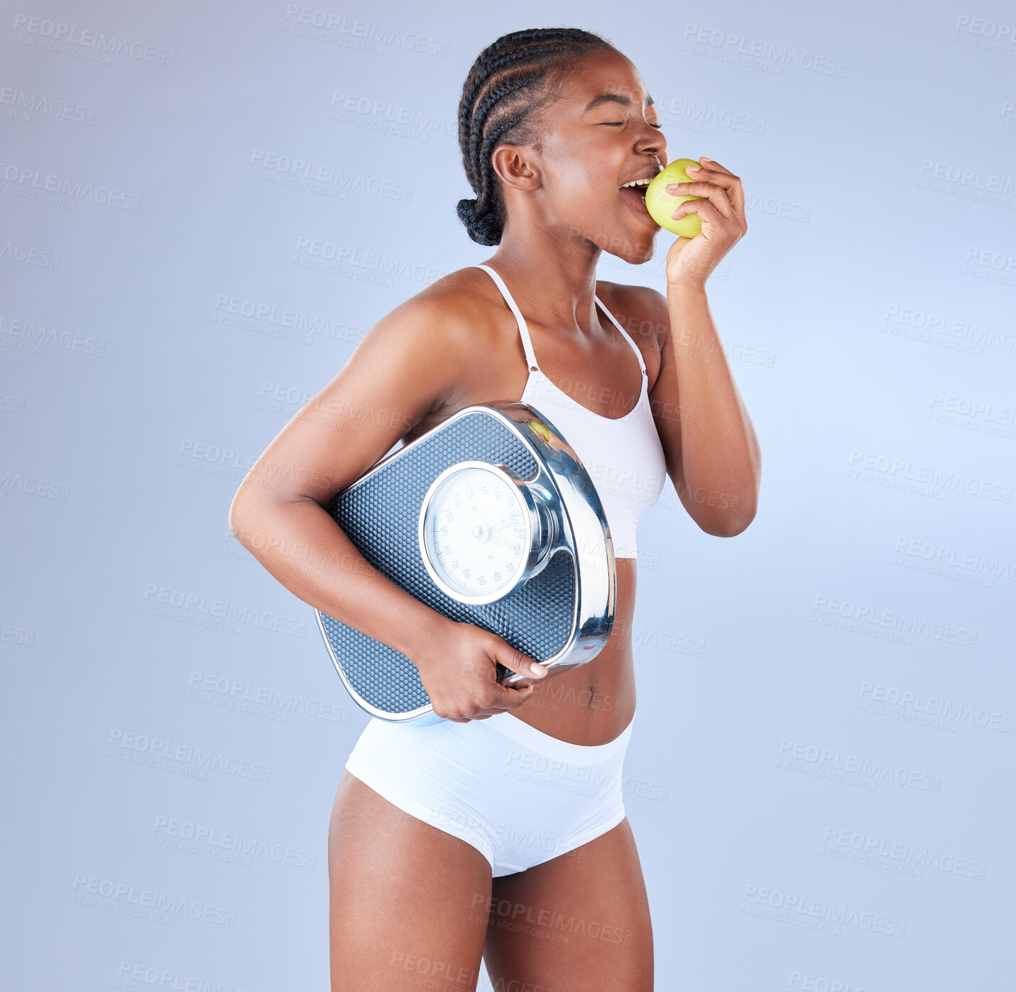 Buy stock photo Happy black woman, scale and bite with apple for diet, nutrition or vitamins on a blue studio background. African, female person or model eating natural green fruit for organic detox or weight loss