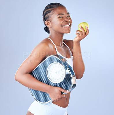 Buy stock photo Studio shot of a young woman eating an apple and holding weighing scale under her arm