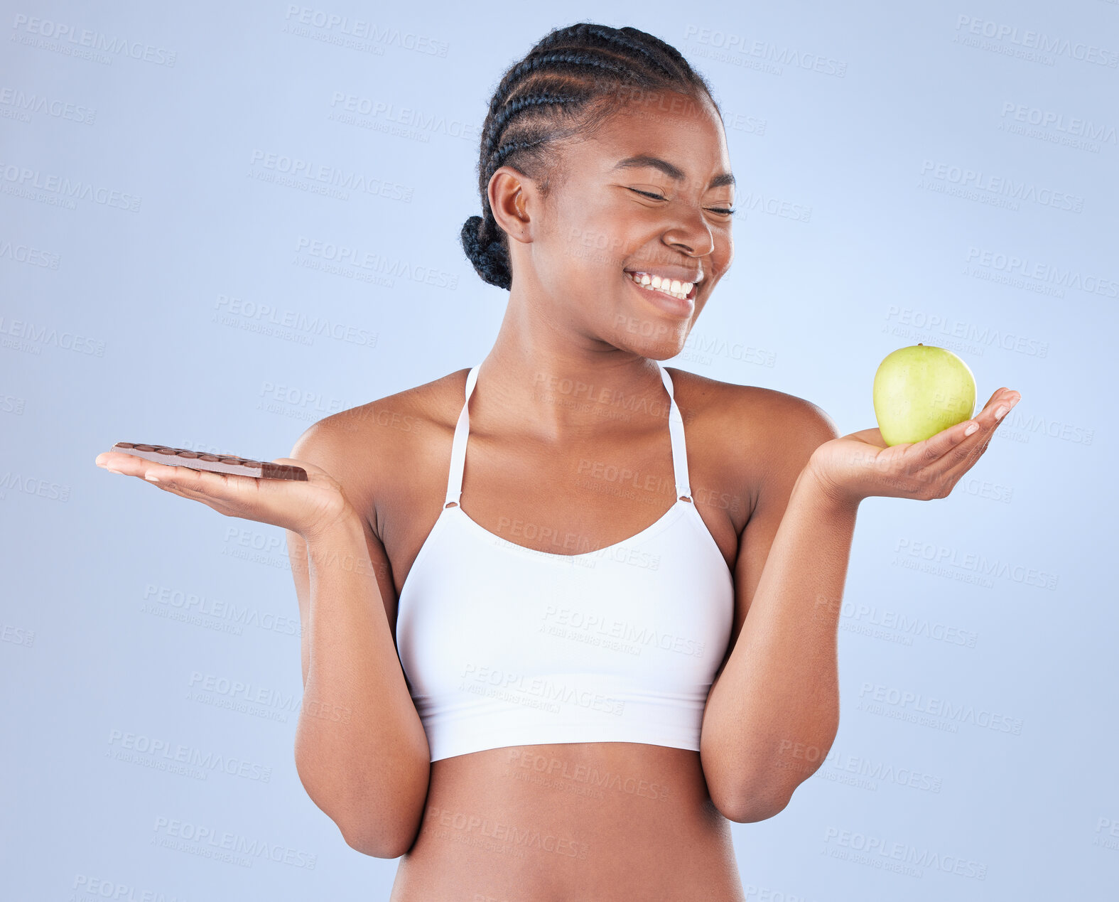 Buy stock photo Studio shot of a young woman holding up a slab of chocolate and an apple in the other hand