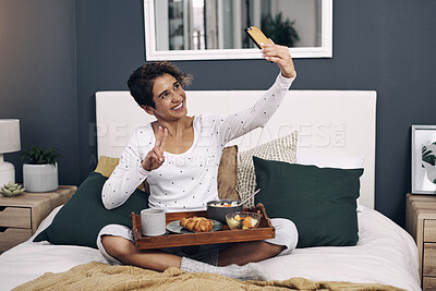 Buy stock photo Shot of a young woman taking a selfie while having breakfast in bed at home