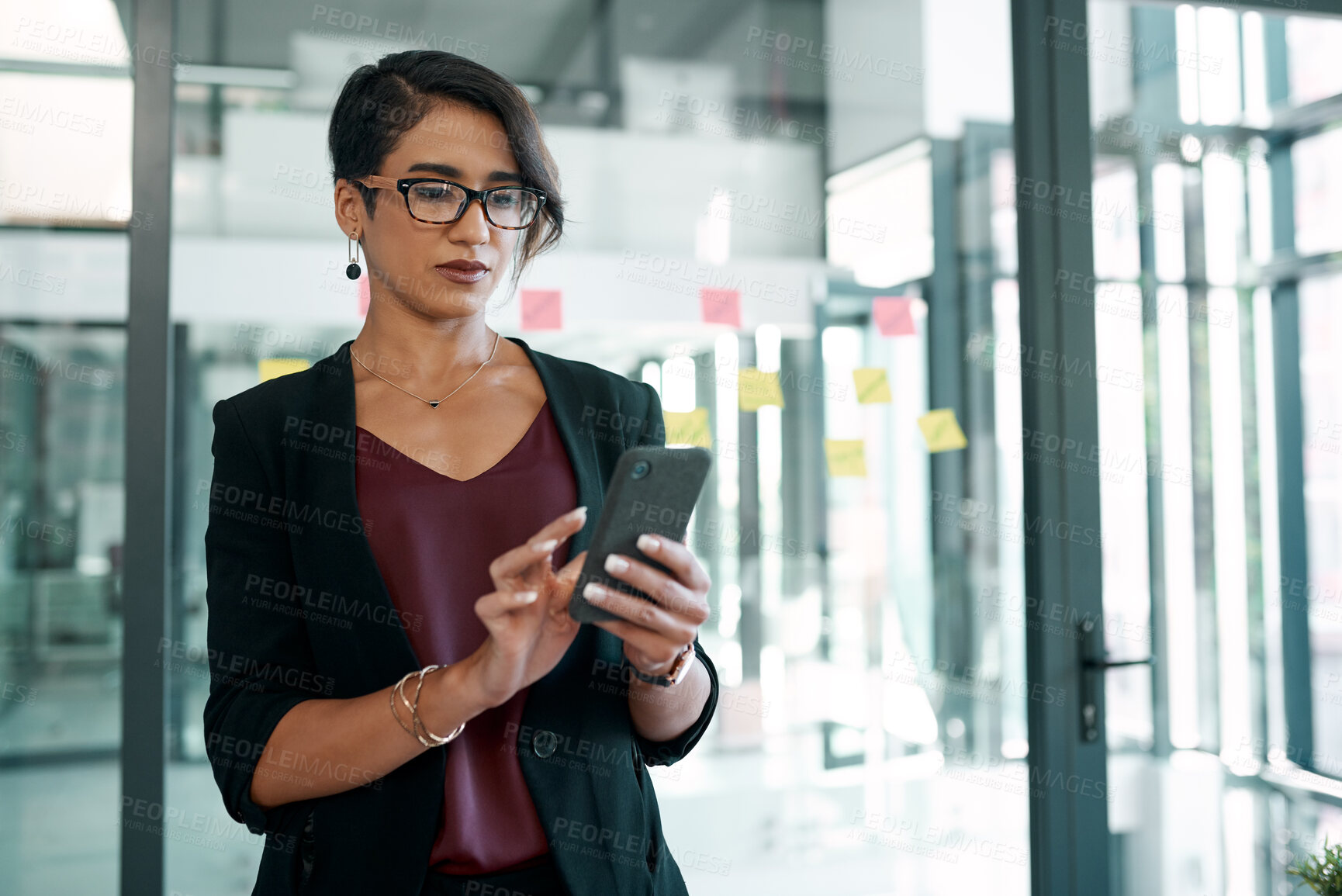 Buy stock photo Shot of an attractive young businesswoman standing alone in the office and using her cellphone
